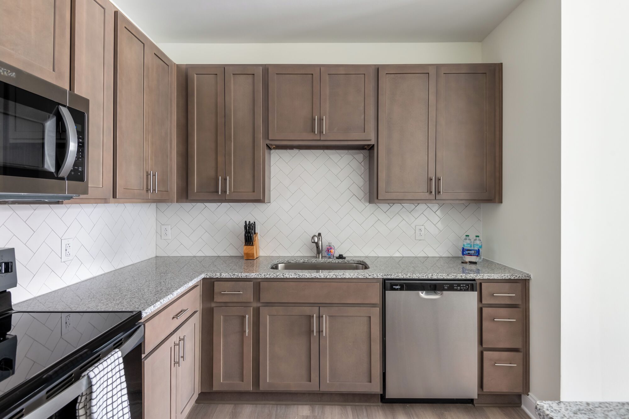 A modern kitchen with wooden cabinets, a stainless steel dishwasher, and a granite countertop.