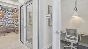 A modern office space with a glass door labeled "WORKSHARE," a meeting table with chairs, and a seating area with a patterned wall and pendant lights.