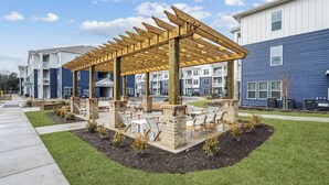 A covered outdoor seating area with chairs and tables, surrounded by a brick patio and small plants.