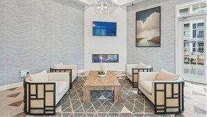 A modern lobby with a herringbone-patterned wall, a large painting, a flat-screen TV, and a seating area with rattan furniture.