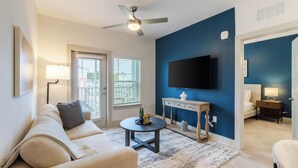 A living room with a sofa, coffee table, and a flat-screen TV mounted on the wall. - Landing Apartments Santa Rosa Beach (Santa Rosa Beach)