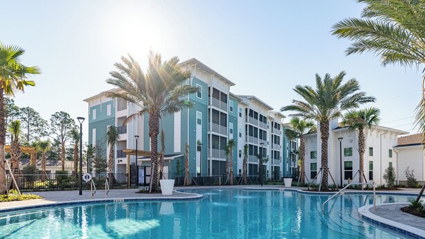 A swimming pool surrounded by multi-story buildings with balconies, palm trees, and a clear sky. - Landing Apartments Santa Rosa Beach (Santa Rosa Beach)