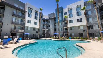 Relax by the central pool surrounded by lounge chairs and umbrellas, with stunning views from the building's balconies and large windows.