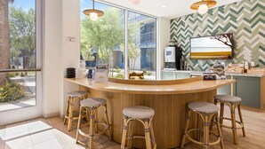 A modern bar area with a curved wooden counter, four wicker stools, and a large window offering a view of the outdoors. - Landing Apartments Glendale (Glendale)