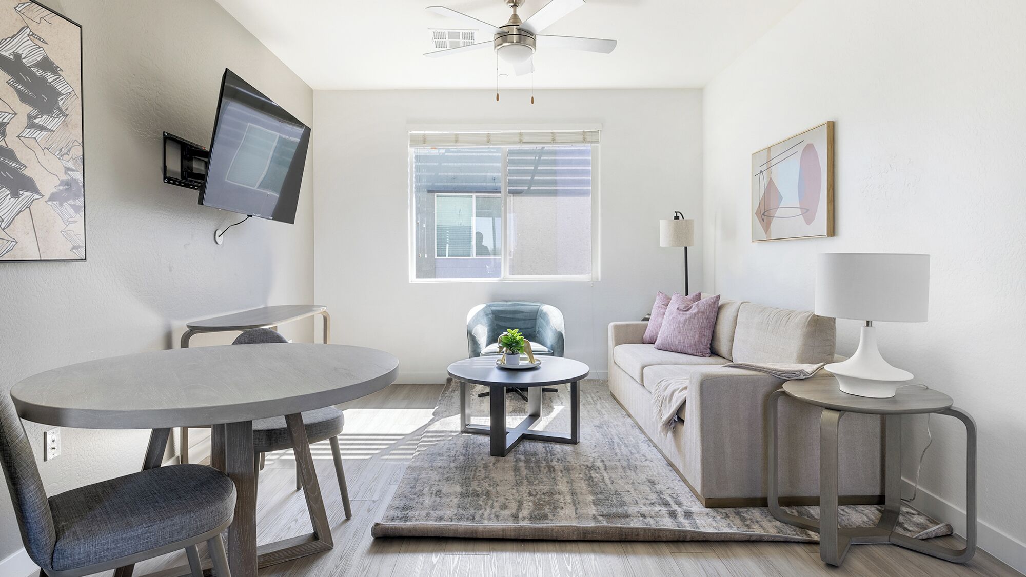 A modern living room with a round dining table, a sofa, a TV mounted on the wall, and a ceiling fan.