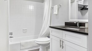 Ein modernes Badezimmer mit einer weißen Badewanne, einer Toilette und einem Waschbecken mit schwarzer Arbeitsplatte.