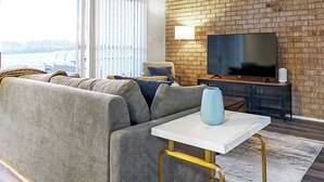 A modern living room with a sectional sofa, a white coffee table, and a flat-screen TV mounted on a brick wall. - Landing Apartments Indy (Indianapolis)