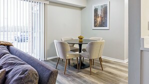 A modern living room with a grey sofa, a dining table with four chairs, and a cityscape view through large windows. - Landing Apartments Indy (Indianapolis)