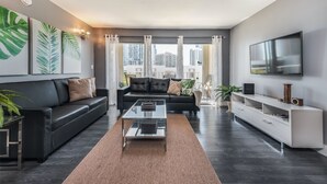 Ett modernt vardagsrum med en svart lädersoffa, ett soffbord i glas och en vit TV-möbel med en platt-TV.