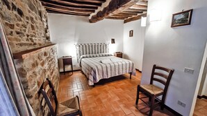 A bedroom with a bed, two chairs, a nightstand, and a stone wall. - La Rocca - Farmhouse La Fattoria (Monte Santa Maria Tiberina)