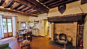 A cozy room with a fireplace, wooden beams, a dining table with chairs, and a kitchen area. - La Rocca - Farmhouse La Fattoria (Monte Santa Maria Tiberina)