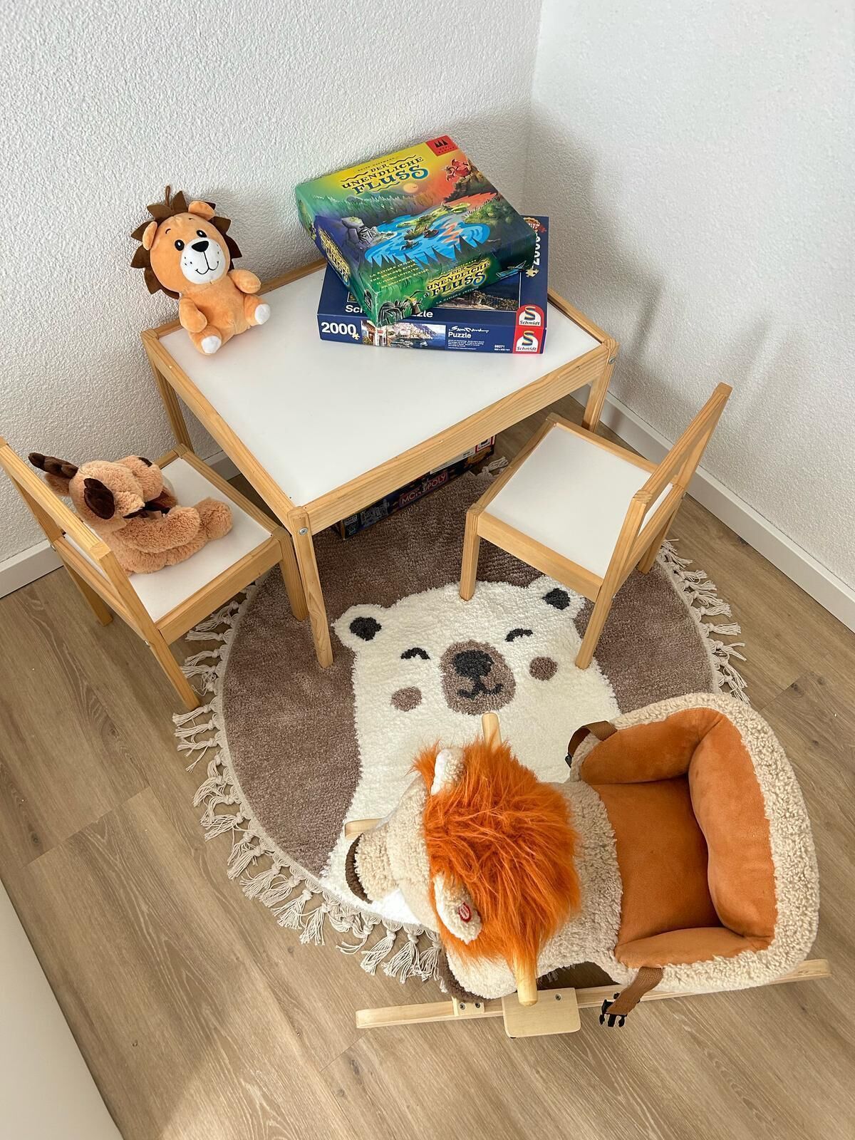 Ein kleiner Holztisch mit einer Knobelbox darauf, umgeben von Kuscheltieren und einem runden Teppich mit Bärenmotiv.