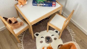 Ein kleiner Holztisch mit einer Knobelbox darauf, umgeben von Kuscheltieren und einem runden Teppich mit Bärenmotiv.