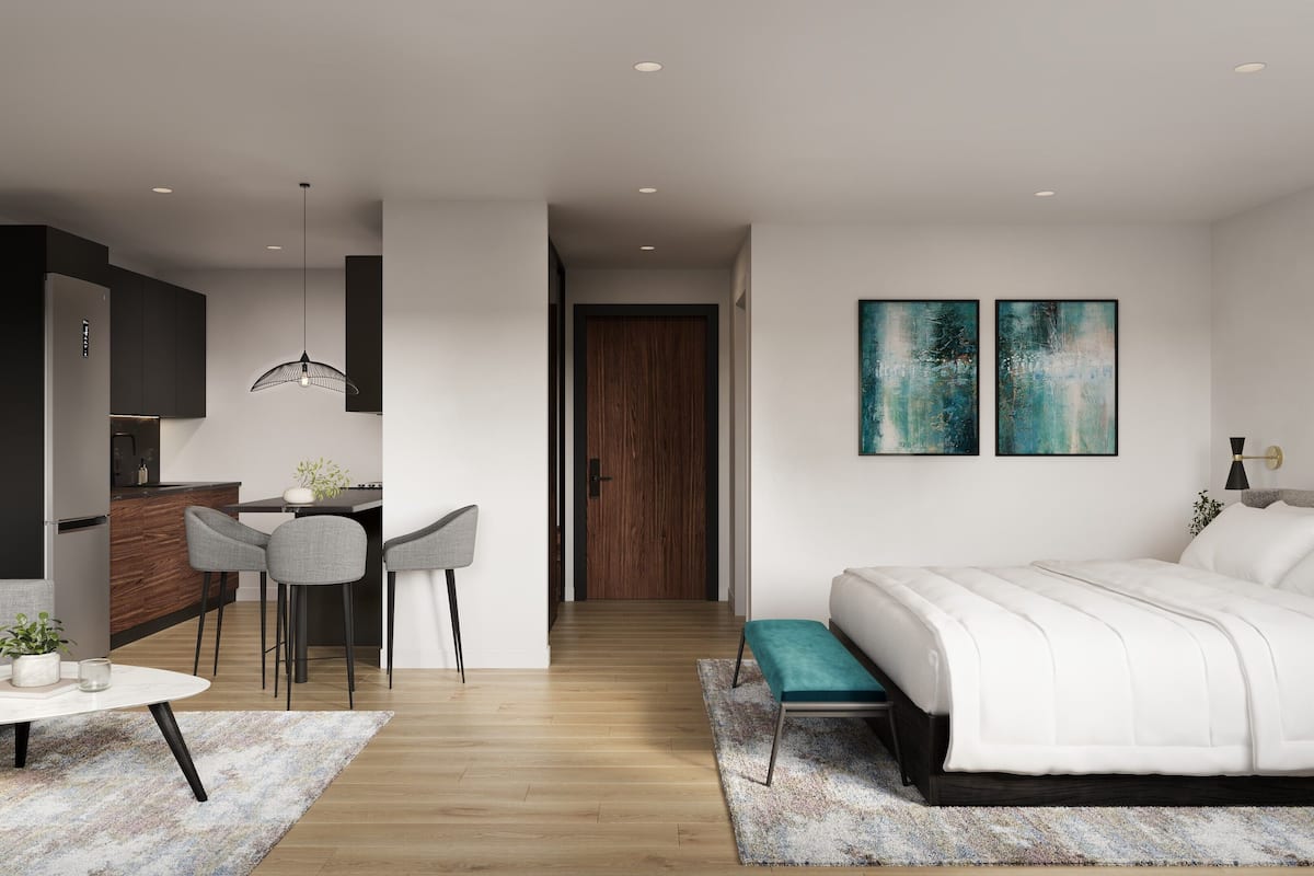 A modern hotel room with a bed, a sofa, a dining area with chairs, and a kitchen area with a refrigerator.