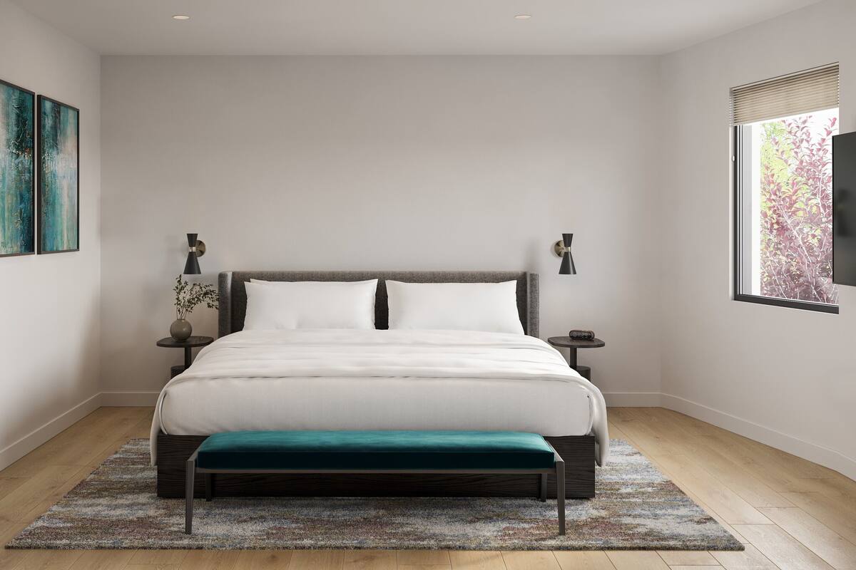 A modern bedroom with a large bed, a bedside table, a small table with a vase, and a window with blinds.
