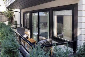 A modern outdoor seating area with a glass railing, wooden furniture, and potted plants. - The Como Hotel (Vancouver)