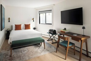 A hotel room with a bed, a desk, a chair, a television, and a window. - The Como Hotel (Vancouver)