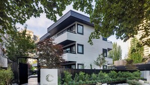Une entrée d’hôtel moderne avec une allée bordée de portails, un panneau indicateur et un jardin aménagé avec des rochers et des arbustes.