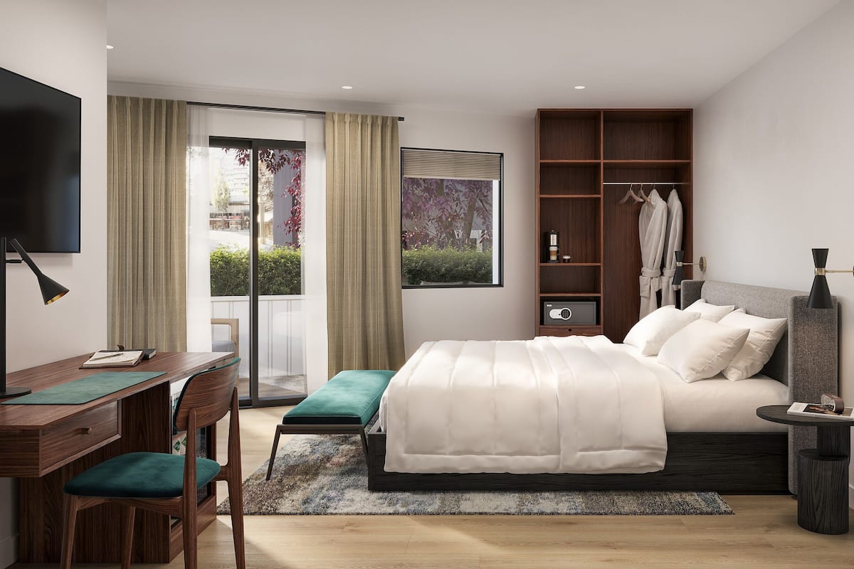 A modern hotel bedroom with a large bed, a desk with a chair, a TV, and a wardrobe.