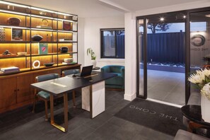 A modern interior with a desk, chairs, a bookshelf, and a glass door leading outside. - The Como Hotel (Vancouver)