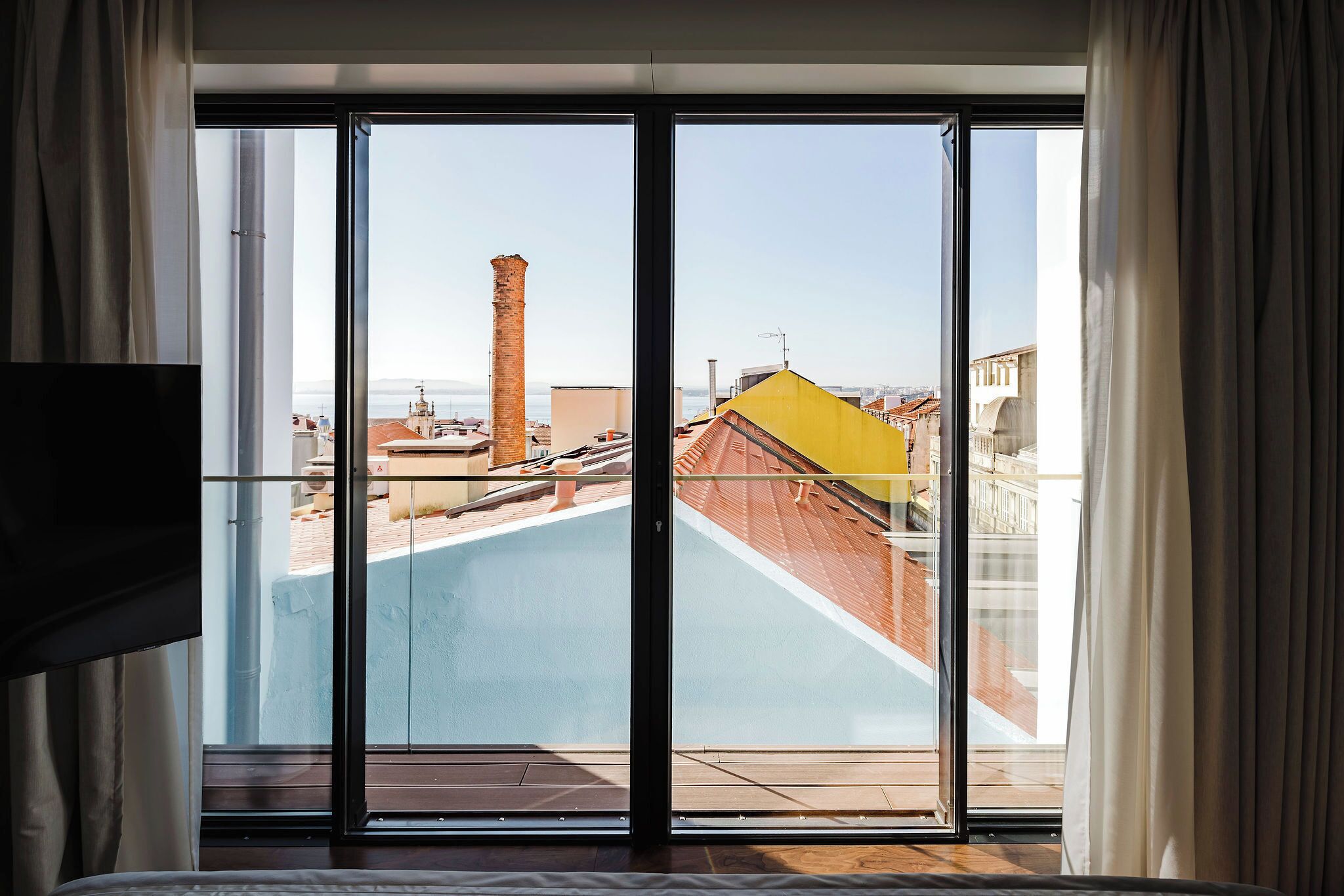 A room with a large sliding glass door leading to a rooftop terrace with a view of buildings and a chimney.