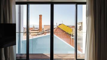 A room with a large sliding glass door leading to a rooftop terrace with a view of buildings and a chimney.