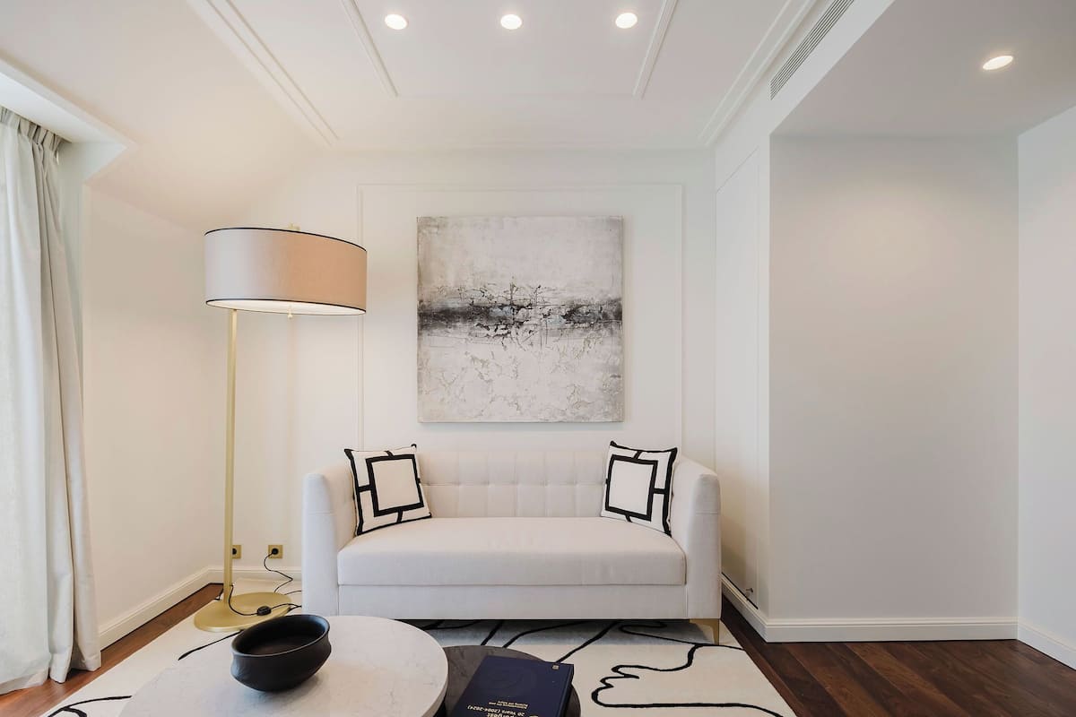 A modern living room with a white sofa, a floor lamp, and a painting on the wall.