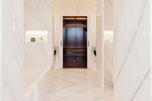 Een moderne lift met een donker interieur en een lichte buitenkant, omringd door marmeren wanden en een vloer in een lichte kleur.
