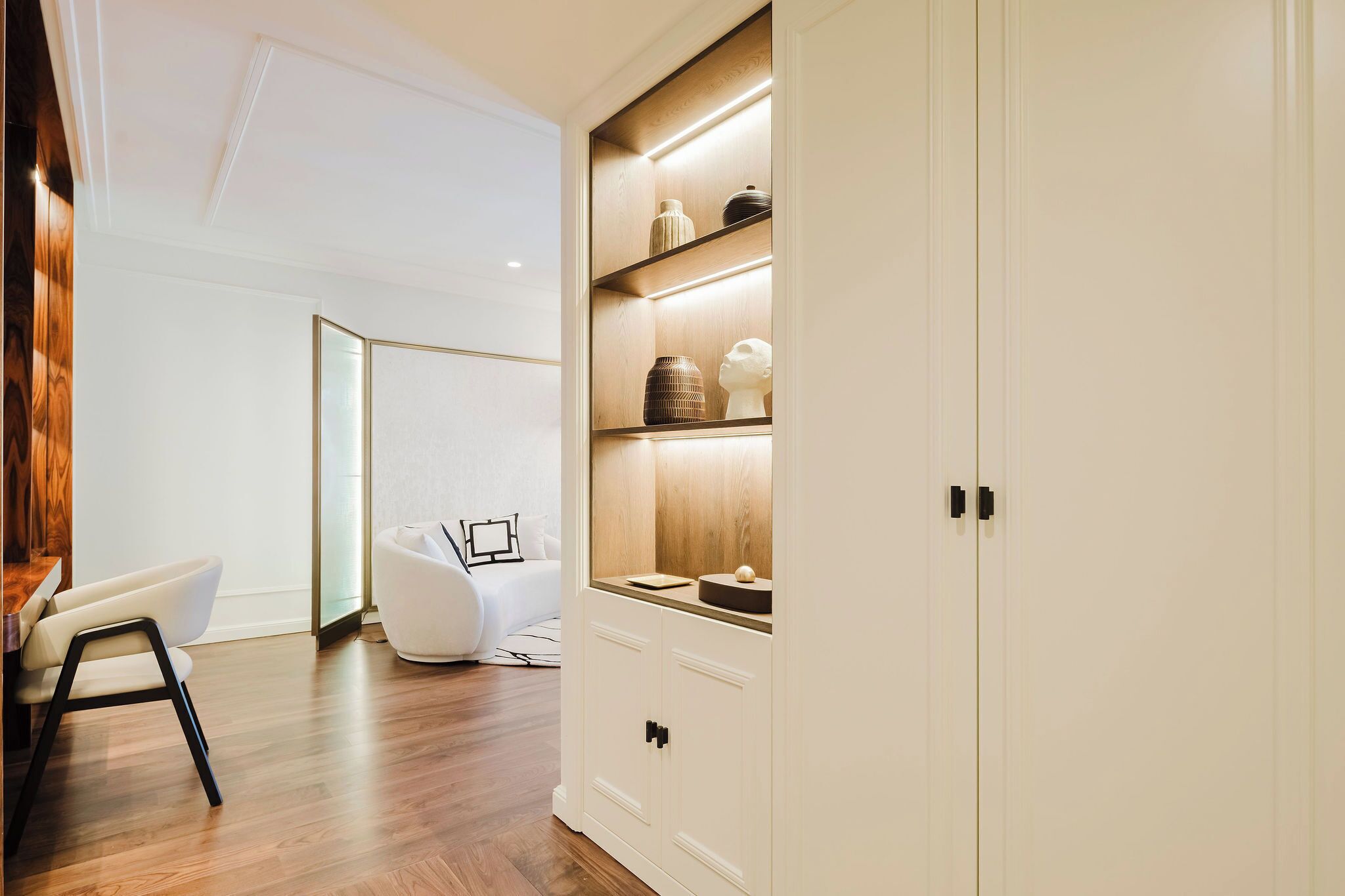 A modern interior with a wooden floor, white walls, and a white wardrobe with shelves.