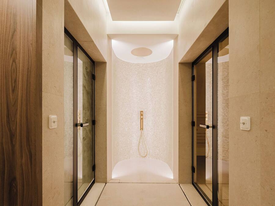 A modern hallway with glass doors, a recessed ceiling, and a shower area.