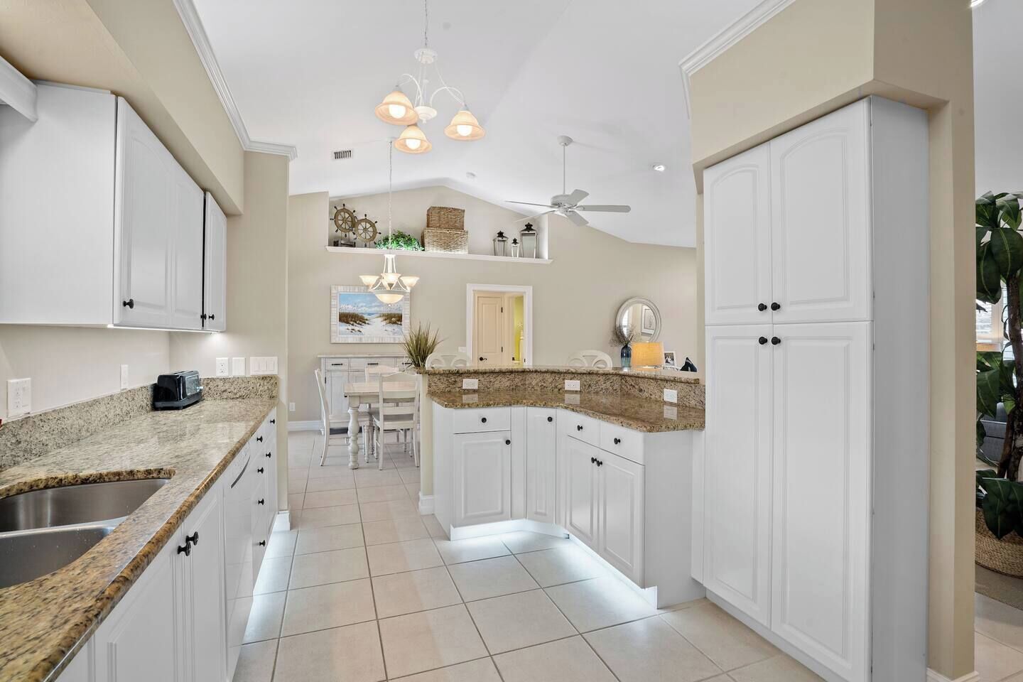 A kitchen with white cabinets, granite countertops, a dining area with a white table and chairs, and a ceiling fan.