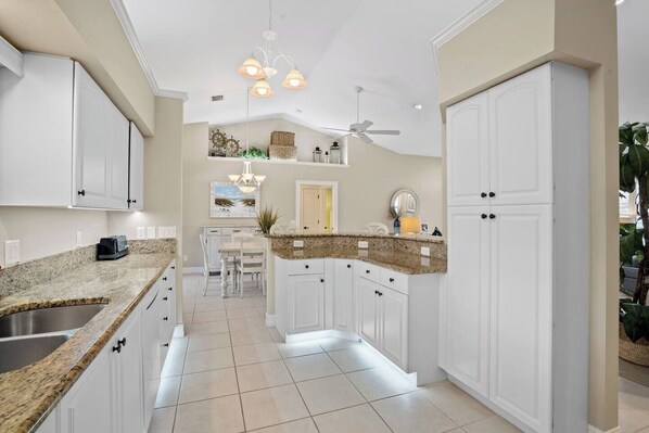 A kitchen with white cabinets, granite countertops, a dining area with a white table and chairs, and a ceiling fan.