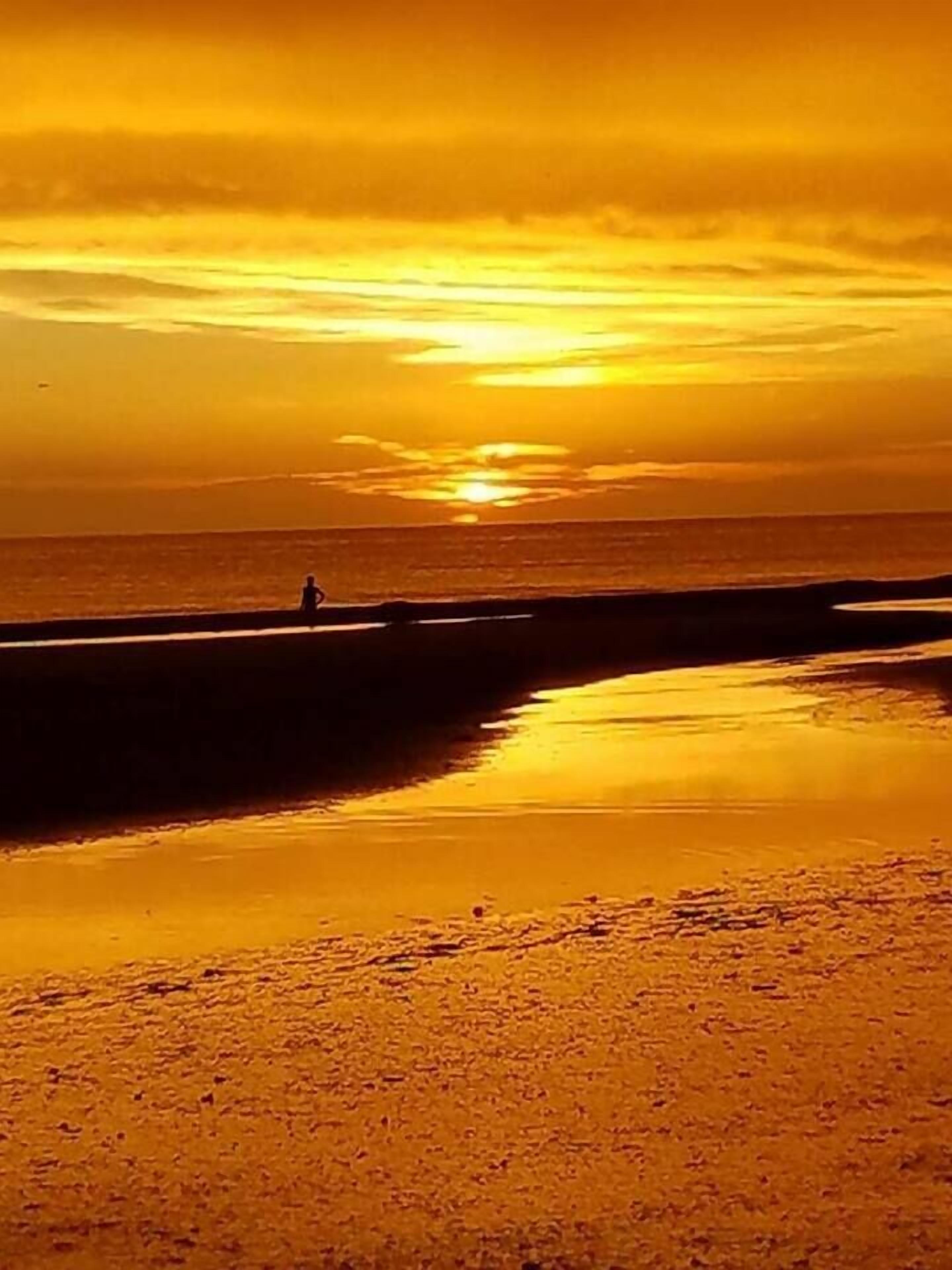 Ein Strandbild mit Sonnenuntergang, ruhiger See und einer Person am Ufer.
