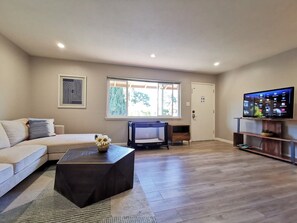 A modern living room with a sofa, a coffee table, a TV, and a window with a view of trees.