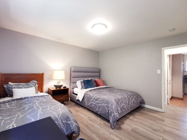 Un dormitorio con dos camas, una mesita de noche con lámpara y una puerta que da a otra habitación.