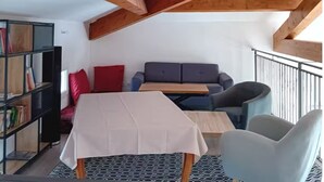 Ein Loft-Zimmer mit freiliegenden Holzbalken, einem Sofa, einem Tisch und einem Bücherregal.