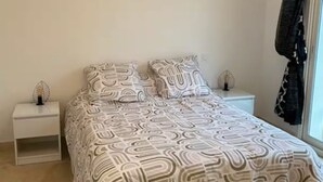 Ein Schlafzimmer mit einem Bett, zwei Nachttischen und einem Fenster mit Vorhängen.