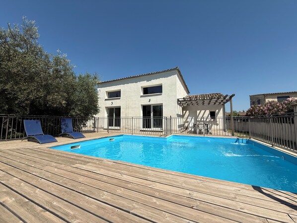 En swimmingpool med ett trädäck, en byggnad med en pergola och ett staket.