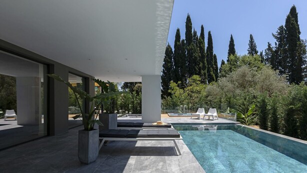 A modern outdoor pool area with a clear view of the surrounding landscape, including tall trees and a well-maintained garden.