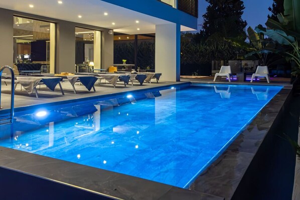 Une piscine extérieure moderne, dotée de chaises longues et d’un espace repas.