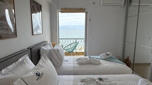 A hotel room with two beds, a balcony with a view of the sea, and a large window.