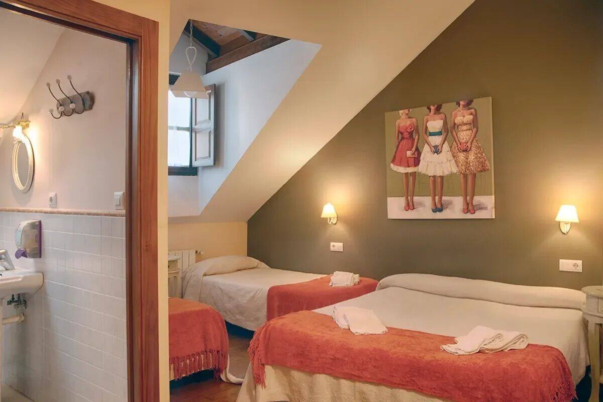Habitación de hotel con dos camas, baño con lavamanos y un cuadro en la pared.