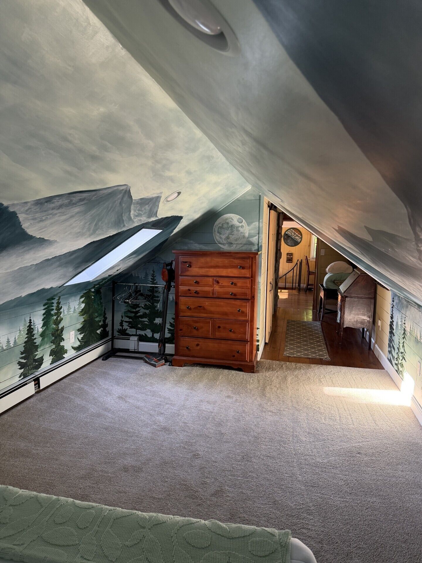 Ein Zimmer mit Wandgemälde von Bergen, einer Holzkommode und einer Tür zu einem weiteren Raum.