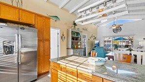 A kitchen with wooden cabinets, a stainless steel refrigerator, and a granite countertop. - Cottage on the Canal with Tiki Bar – Relax & Unwind in Ocean Isle (Ocean Isle Beach)