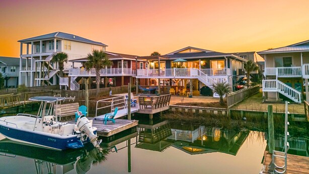 A waterfront property with multiple houses, docks, and a boat. - Cottage on the Canal with Tiki Bar – Relax & Unwind in Ocean Isle (Ocean Isle Beach)