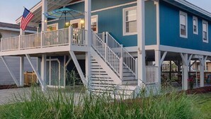 A two-story house with a covered porch, a staircase, and a flag. - Cottage on the Canal with Tiki Bar – Relax & Unwind in Ocean Isle (Ocean Isle Beach)