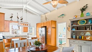 A spacious kitchen with wooden cabinets, a dining table, and a ceiling fan. - Cottage on the Canal with Tiki Bar – Relax & Unwind in Ocean Isle (Ocean Isle Beach)