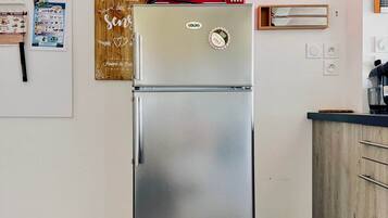 Ein Edelstahl-Kühlschrank mit Gefrierfach, darüber eine Mikrowelle und ein hölzernes Schild mit Schriftzug an der Wand.