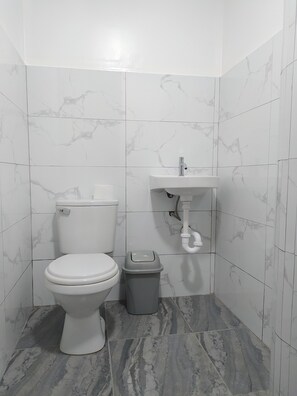 Pieni, moderni kylpyhuone, jossa on wc, pesuallas ja roskakori.