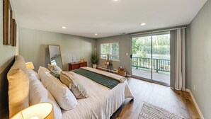 A bedroom with a large bed, a dresser, a mirror, and a window with a view of a balcony.